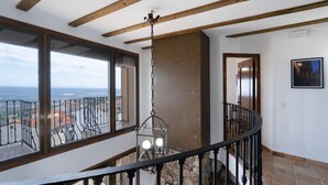 Une pièce aux hauts plafonds, avec des poutres apparentes en bois, un mur en pierre et une vue sur le paysage urbain, visible à travers de grandes fenêtres.