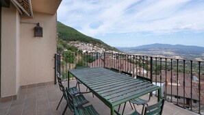 Un balcon avec une table et des chaises, d’où l’on peut admirer la ville et les montagnes au loin.