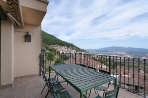 A balcony with a table and chairs, overlooking a town and distant mountains.