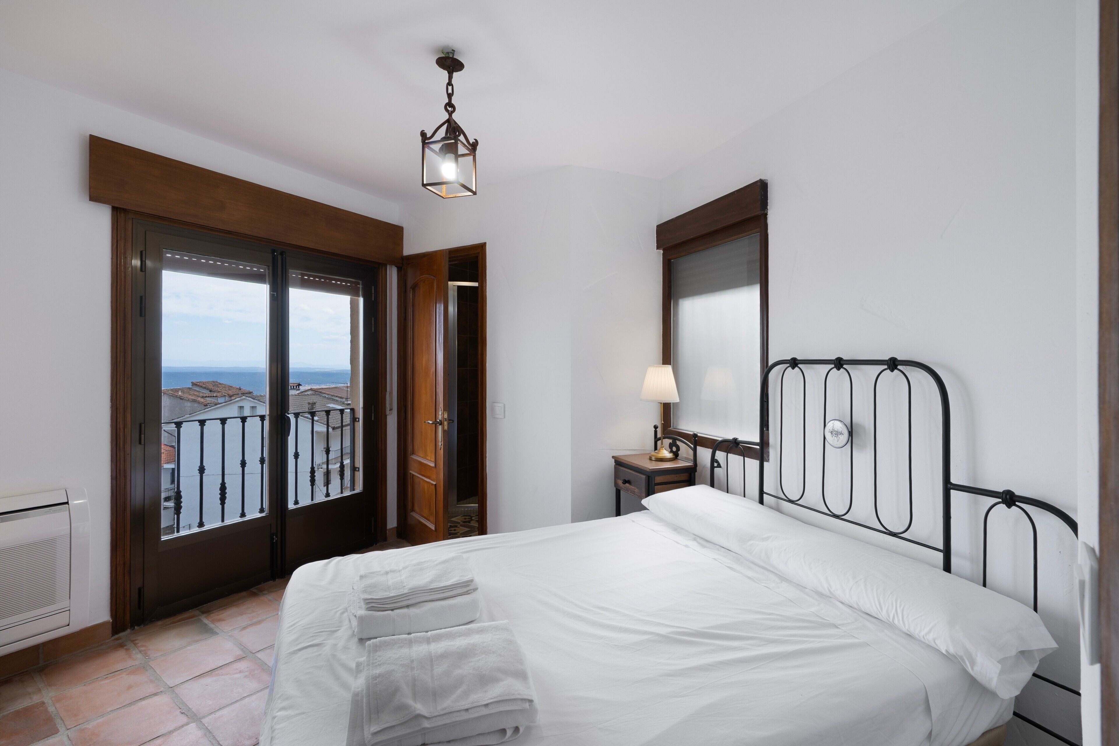 A hotel room with a bed, a nightstand, a lamp, a window with a view, and a door.