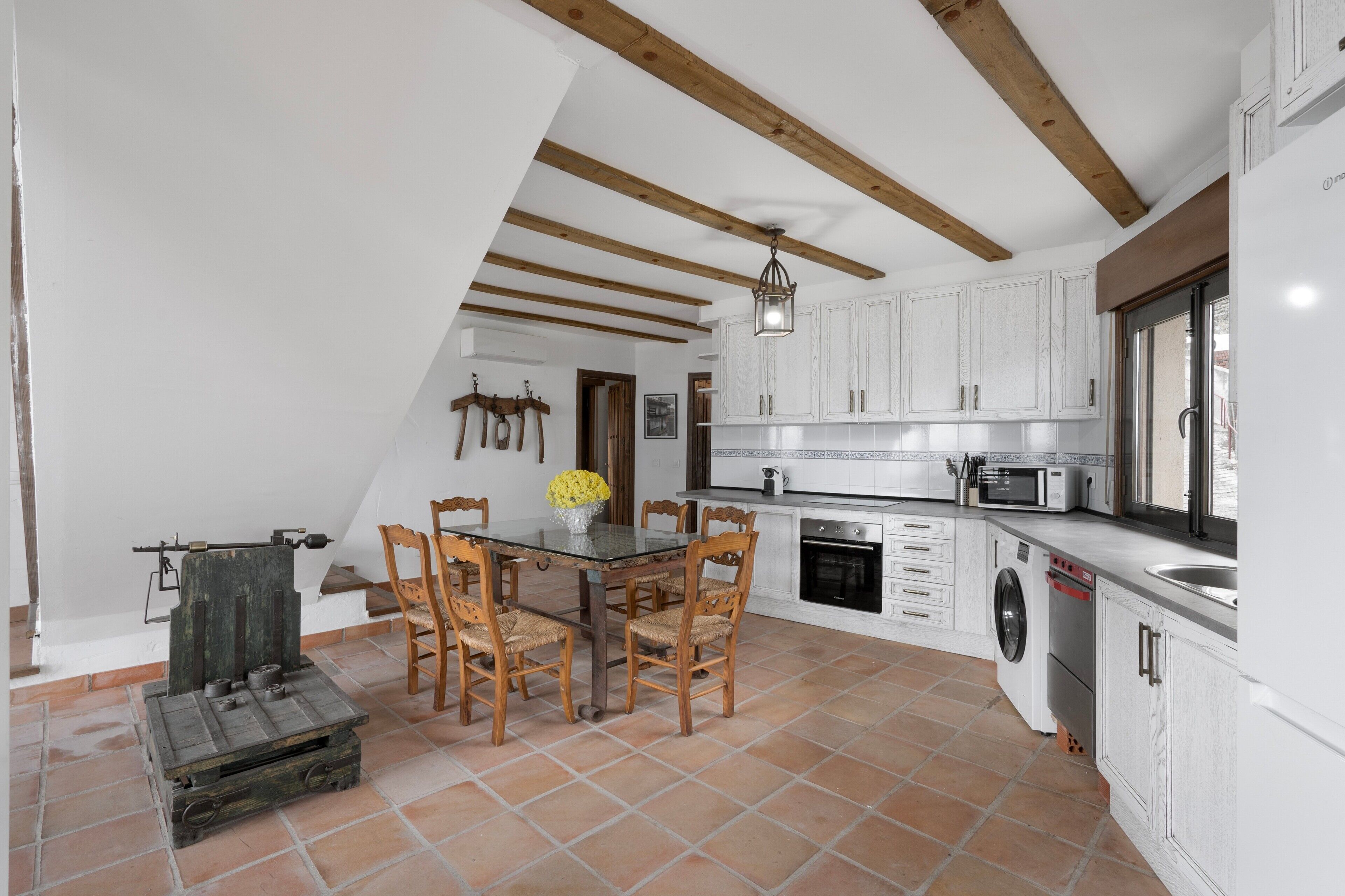 A kitchen with white cabinets, a dining table with chairs, a hanging lantern, and a washing machine.