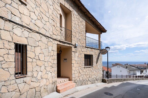A stone building with a balcony, a small entrance, and a view of the sea.