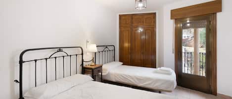 Un dormitorio con dos camas individuales, una mesita de noche con lámpara, un armario y una puerta que da a un área exterior.