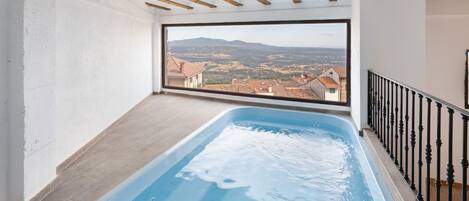 A balcony with a view of a valley and mountains, a swimming pool, and a wooden ceiling.