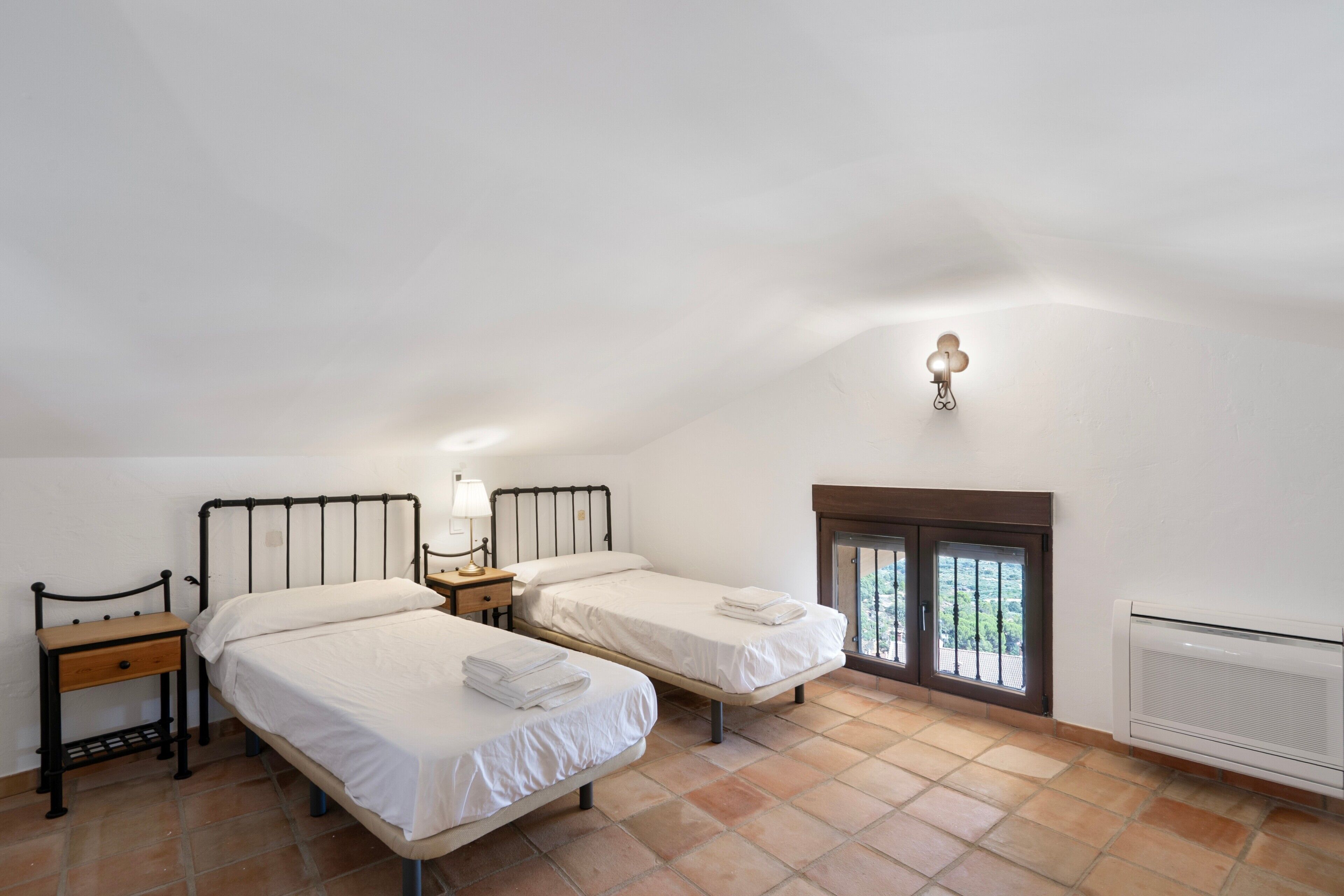 Ein Schlafzimmer mit zwei Betten, einem Nachttisch, einer Lampe und einem Fenster mit Blick.