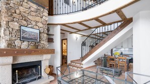 Un intérieur spacieux agrémenté d’une cheminée en pierre, d’un escalier en bois et d’une balustrade en verre donnant sur un coin repas.