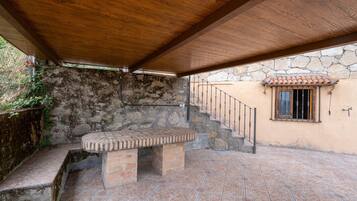 A covered patio area with a brick table, stone wall, and a staircase leading to a window.