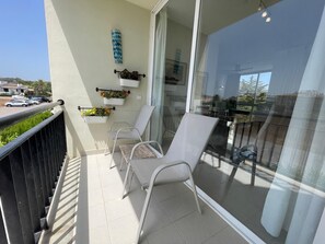 Ein Balkon mit zwei weißen Stühlen, einem Metallgeländer und einer Glastür, die auf eine Terrasse führt.