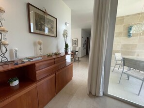 Ein modernes Wohnzimmer mit einem Holzkabinett, einem Essbereich mit Tisch und Stühlen sowie einem großen Fenster mit Vorhängen.
