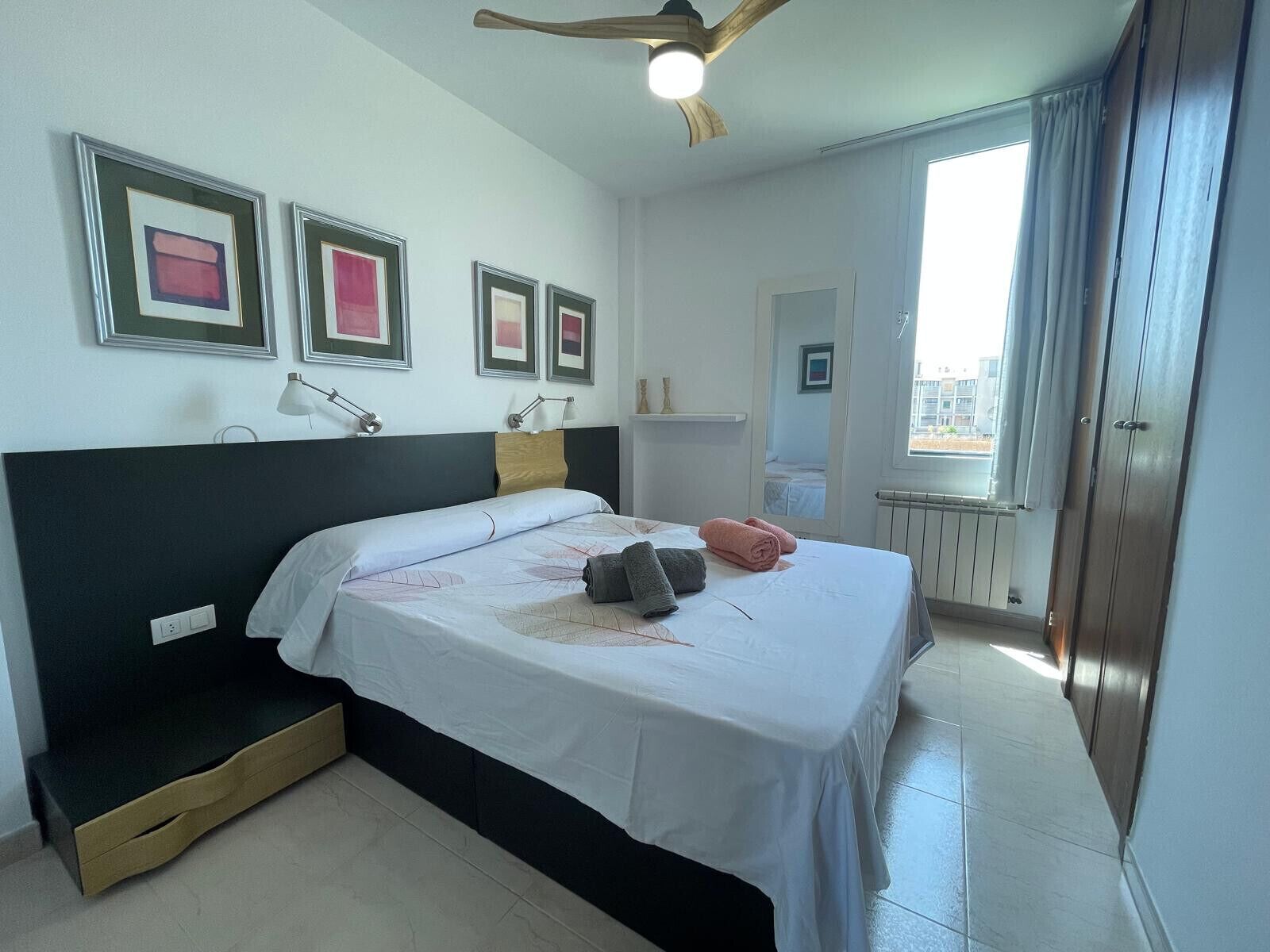 A hotel room with a bed, bedside tables, a ceiling fan, and a window with curtains.