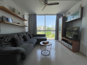 Ein modernes Wohnzimmer mit einem Ecksofa, einem Fernseher und einem Deckenventilator.