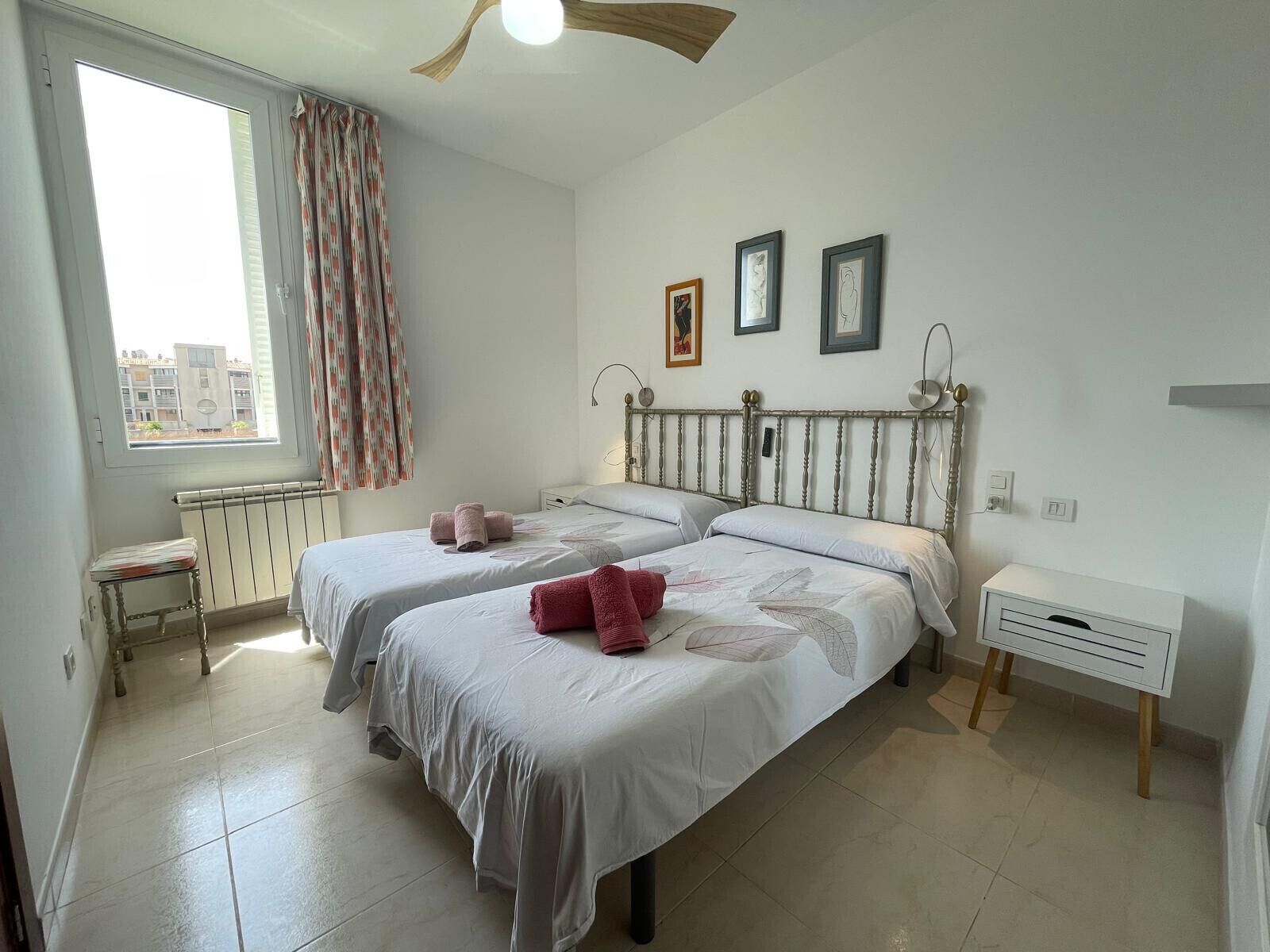Un dormitorio con dos camas, un radiador, una ventana con cortinas y una mesita de noche.