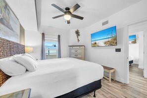 Ein Schlafzimmer mit einem Bett, einem Deckenventilator, einem Schminktisch, einer Bank und einem an der Wand befestigten Fernseher.