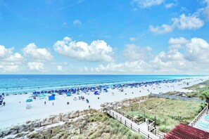 Una spiaggia con una passerella di legno che conduce alla riva, sabbia fine e un cielo azzurro terso.