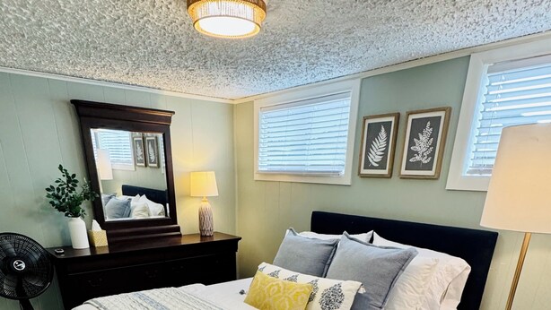 Une chambre à coucher avec un lit, des tables de chevet, un miroir et un ventilateur de plafond.