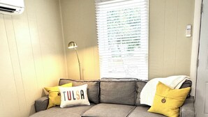 Un salon comprenant un canapé d’angle, un pouf et un climatiseur fixé au mur.