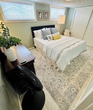 Un dormitorio con cama, mesita de noche, lámpara y una planta en maceta.