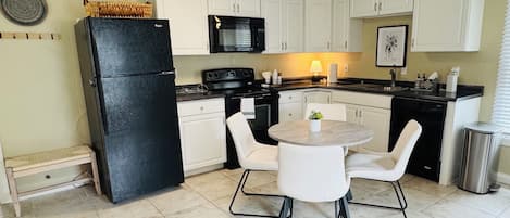 A compact kitchen with white cabinets, a black refrigerator, a microwave, a stove, and a dining table with chairs.