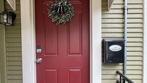 Une porte rouge ornée d’une guirlande, une boîte aux lettres et une petite marche menant à l’entrée.