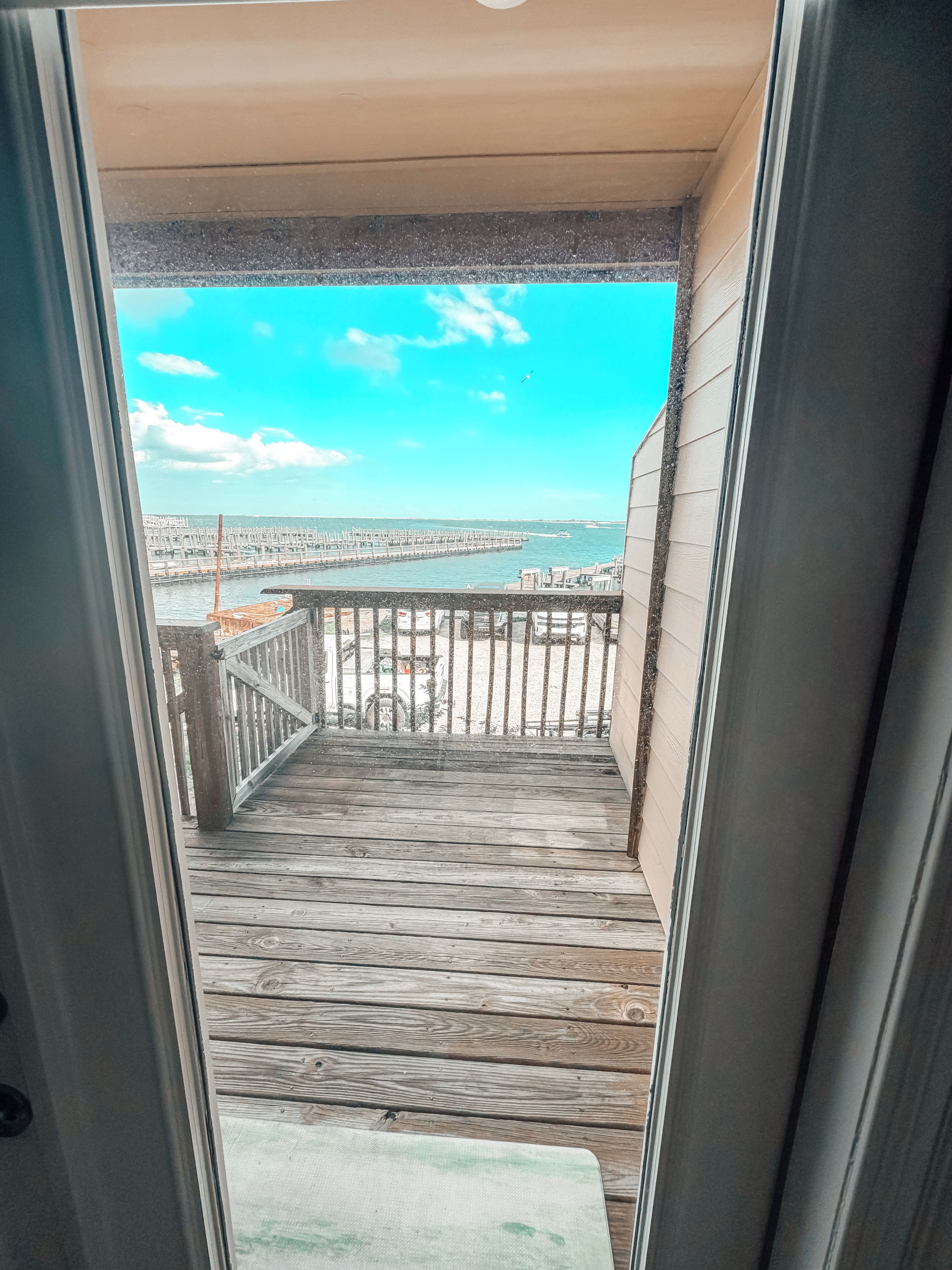 Una terraza de madera que lleva a un balcón con vistas a un puerto deportivo y un paisaje urbano distante.