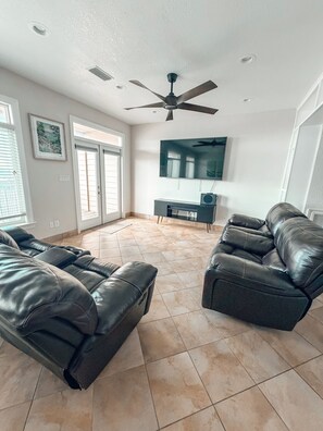 A living room with a ceiling fan, a flat-screen TV, and two leather sofas. - Waterfront Getaway (Pensacola)