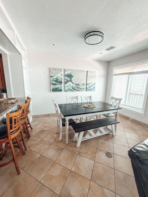 A dining area with a table and chairs, a tiled floor, and a window with blinds. - Waterfront Getaway (Pensacola)