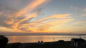 A sunset over a calm body of water with a beach and a small building. - NOW BOOKING FOR 2027!! (Irish Cove)