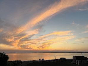 Ein Sonnenuntergang über ruhigem Wasser mit einem Strand und einem kleinen Gebäude.