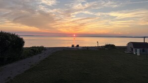 A sunset over a calm body of water with a grassy area, a small shed, and a couple of chairs facing the view. - NOW BOOKING FOR 2027!! (Irish Cove)