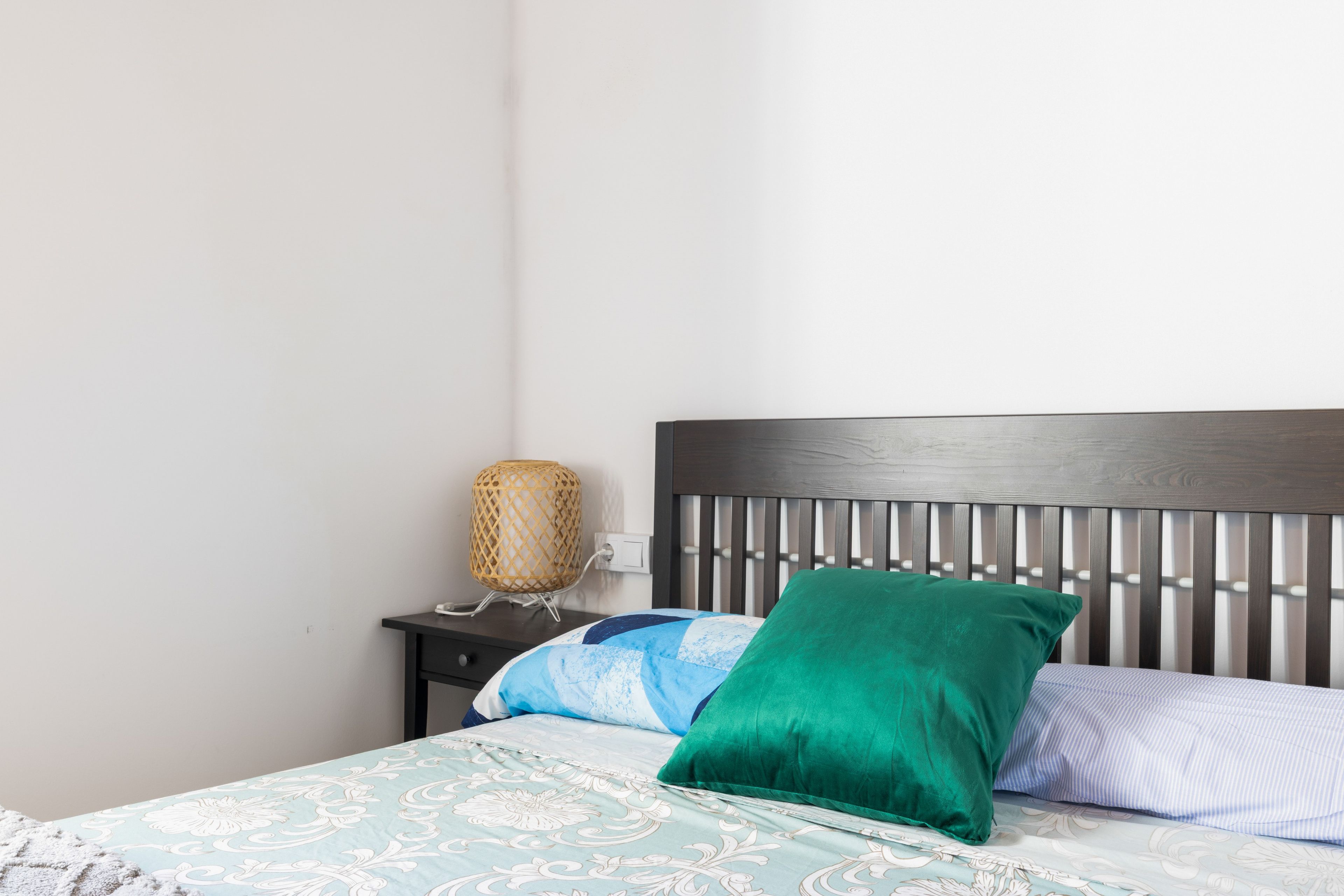 A neatly made bed with a patterned bedspread and pillows, a bedside lamp, and a dark wooden headboard.