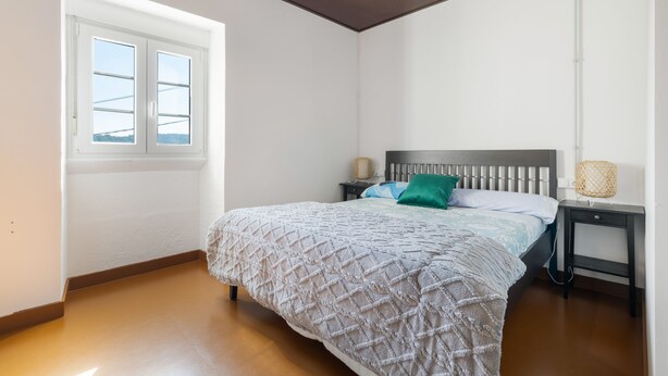 A bedroom with a bed, a nightstand, a lamp, and a window.