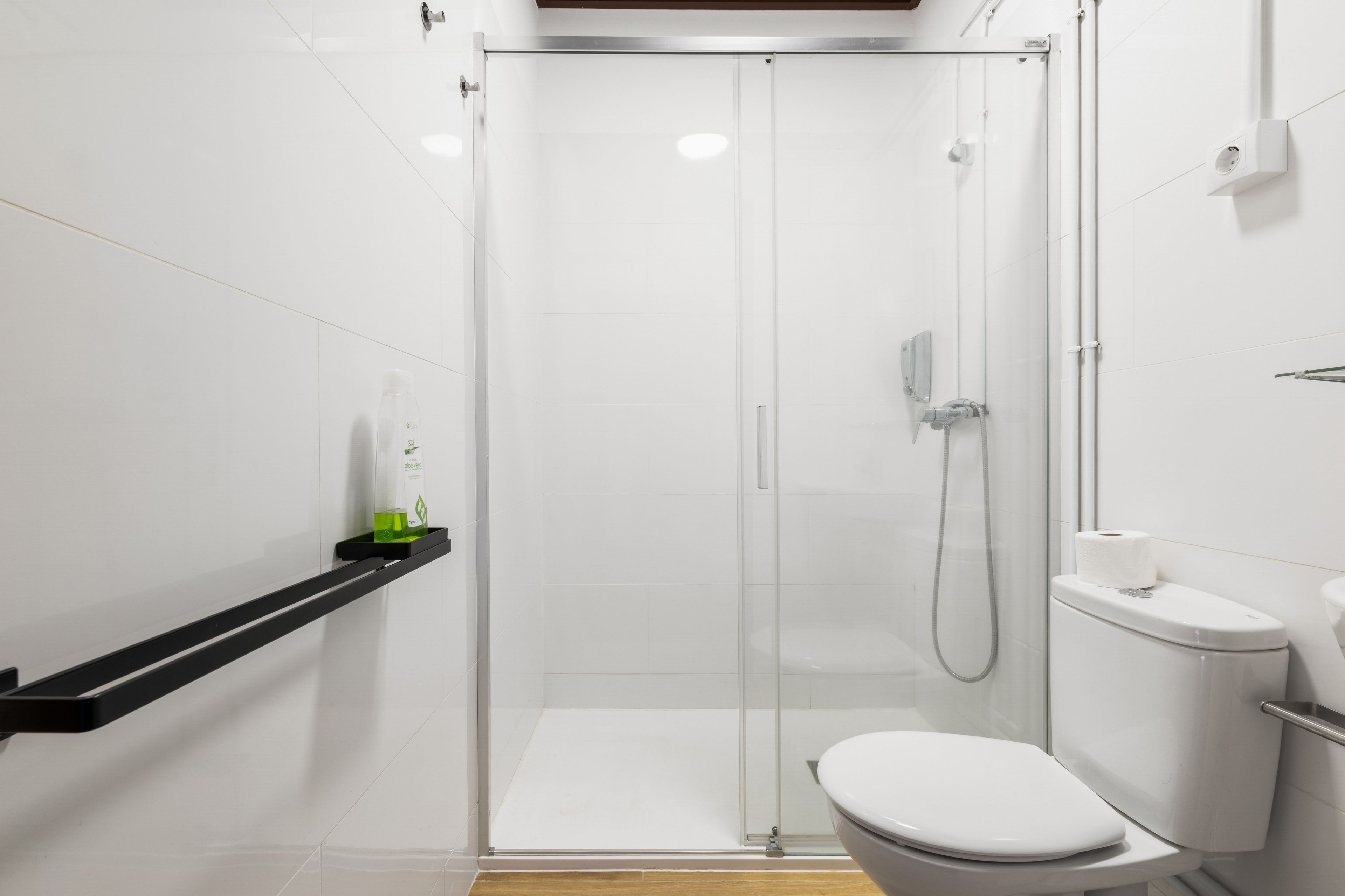 Un baño moderno con ducha envuelta en vidrio, inodoro blanco y un estante con artículos de tocador.
