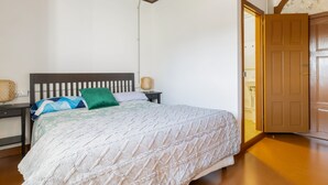 A bedroom with a bed, bedside tables, a lamp, and a door leading to another room.