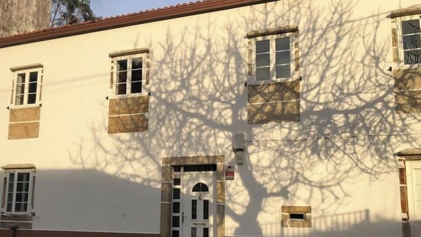 Un edifici amb façana blanca, diverses finestres i una porta amb un petit finestró a la part superior.