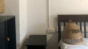 Habitació amb un llit, una taula petita, una làmpada penjada a la paret i una presa de corrent.