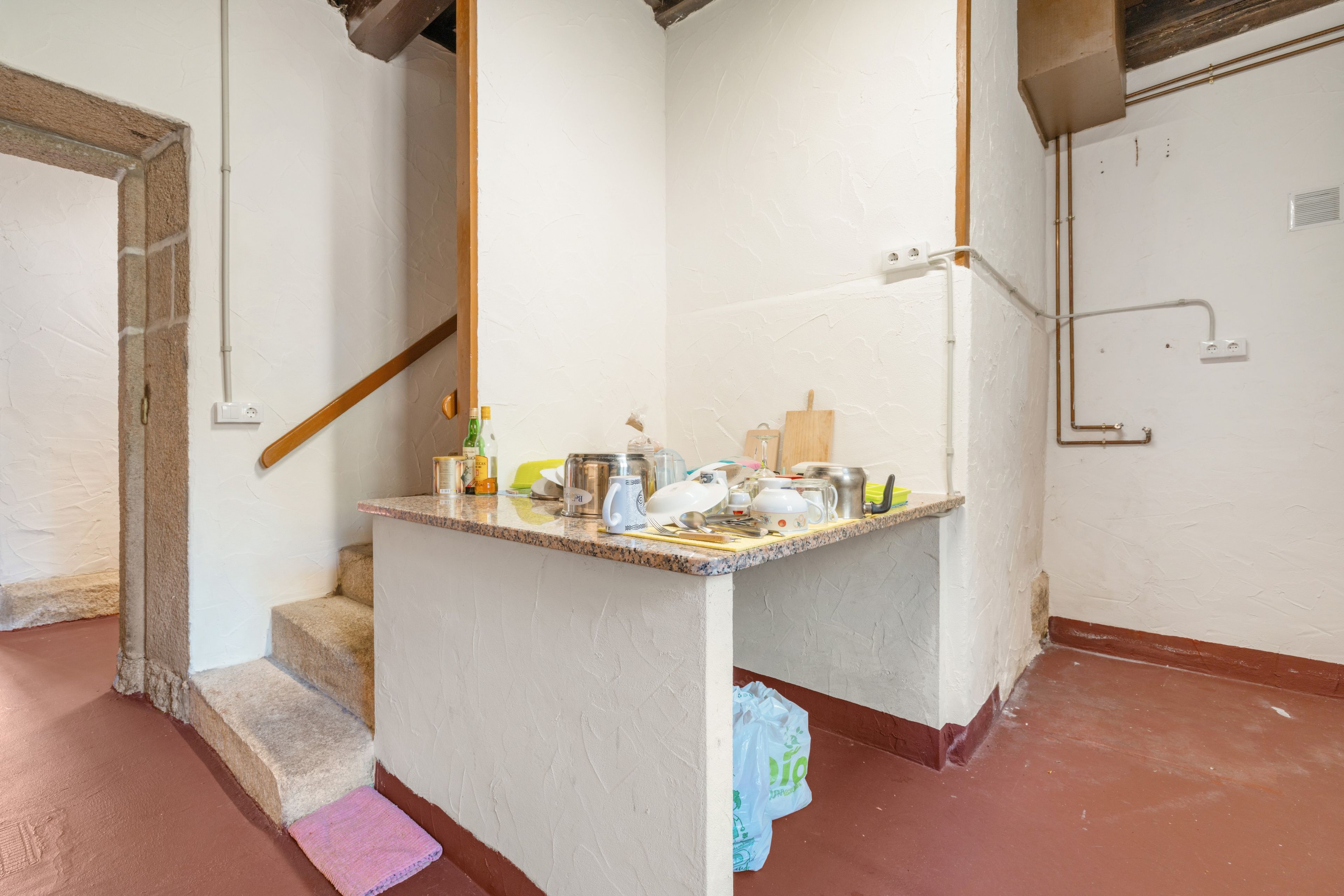 Un pequeño espacio tipo cocina con una encimera, diversos utensilios y una escalera de madera.