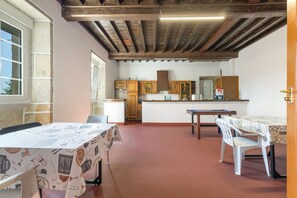 A dining area with a table set for two, a kitchen in the background, and a wooden ceiling.