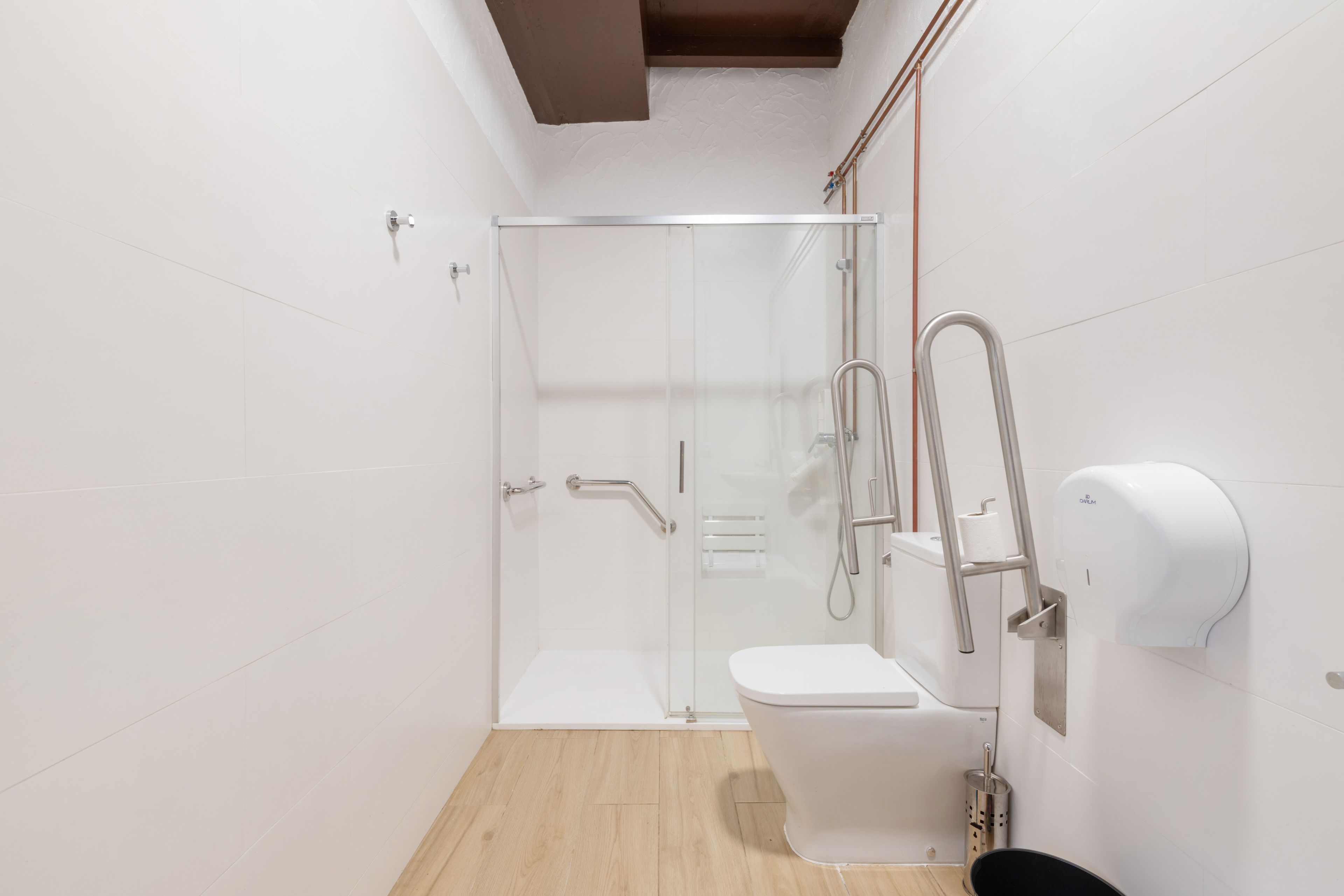 Un baño moderno con cabina de ducha de vidrio, inodoro y secamanos.
