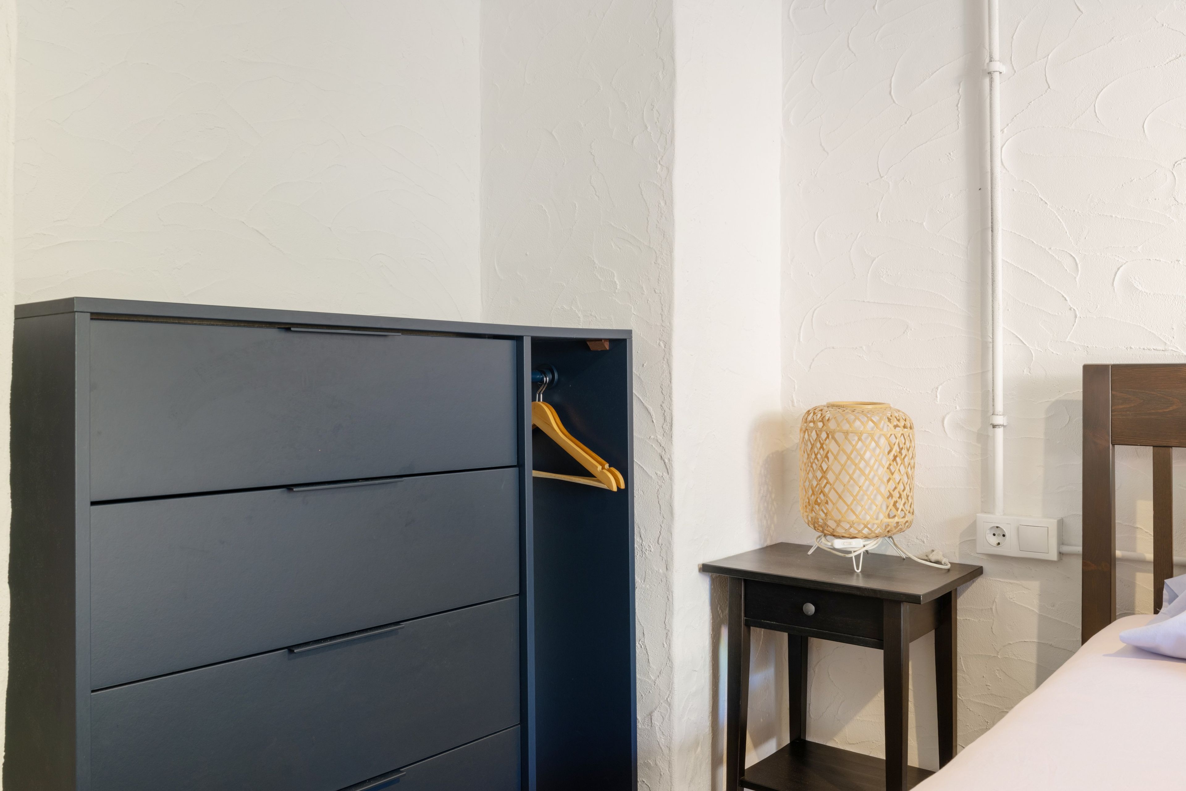 Una habitación con un armario azul oscuro, una mesita de noche pequeña con una lámpara y una mesita de madera.