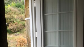 Porta blanca amb un panell de vidre mat i un mànec, que dona pas a una zona exterior amb un camí de formigó i vegetació.