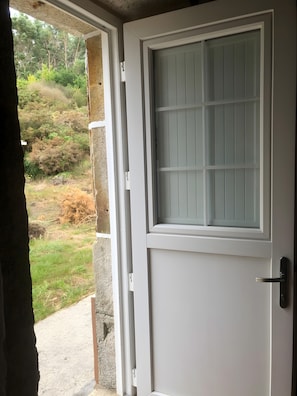 A white door with a frosted glass panel and a handle, leading to an outdoor area with a concrete path and greenery. - Adapted Room with Mountain Views, Shared Terrace and WiFi (Moraime)