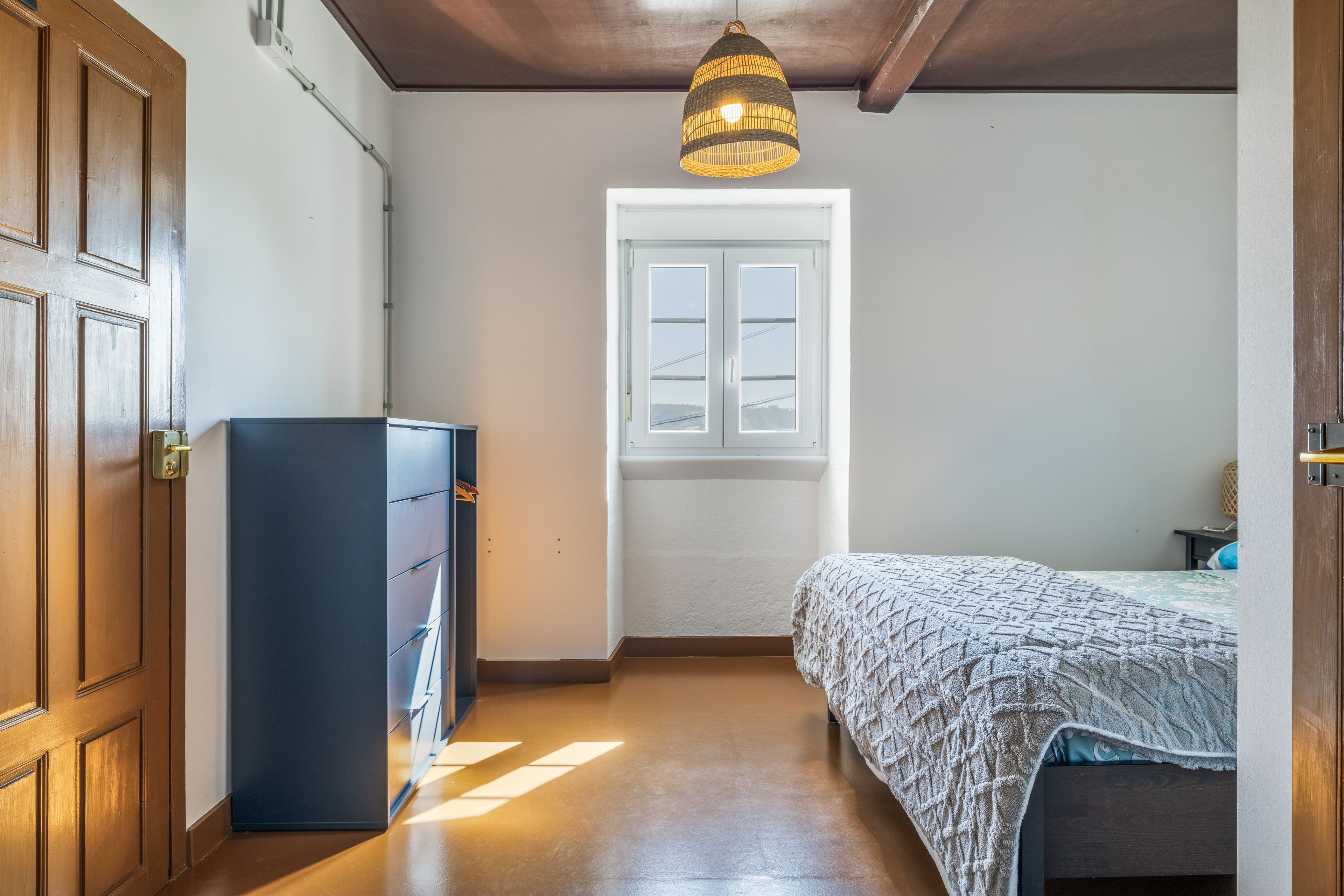 Un dormitorio con cama, armario, ventana y lámpara colgante.