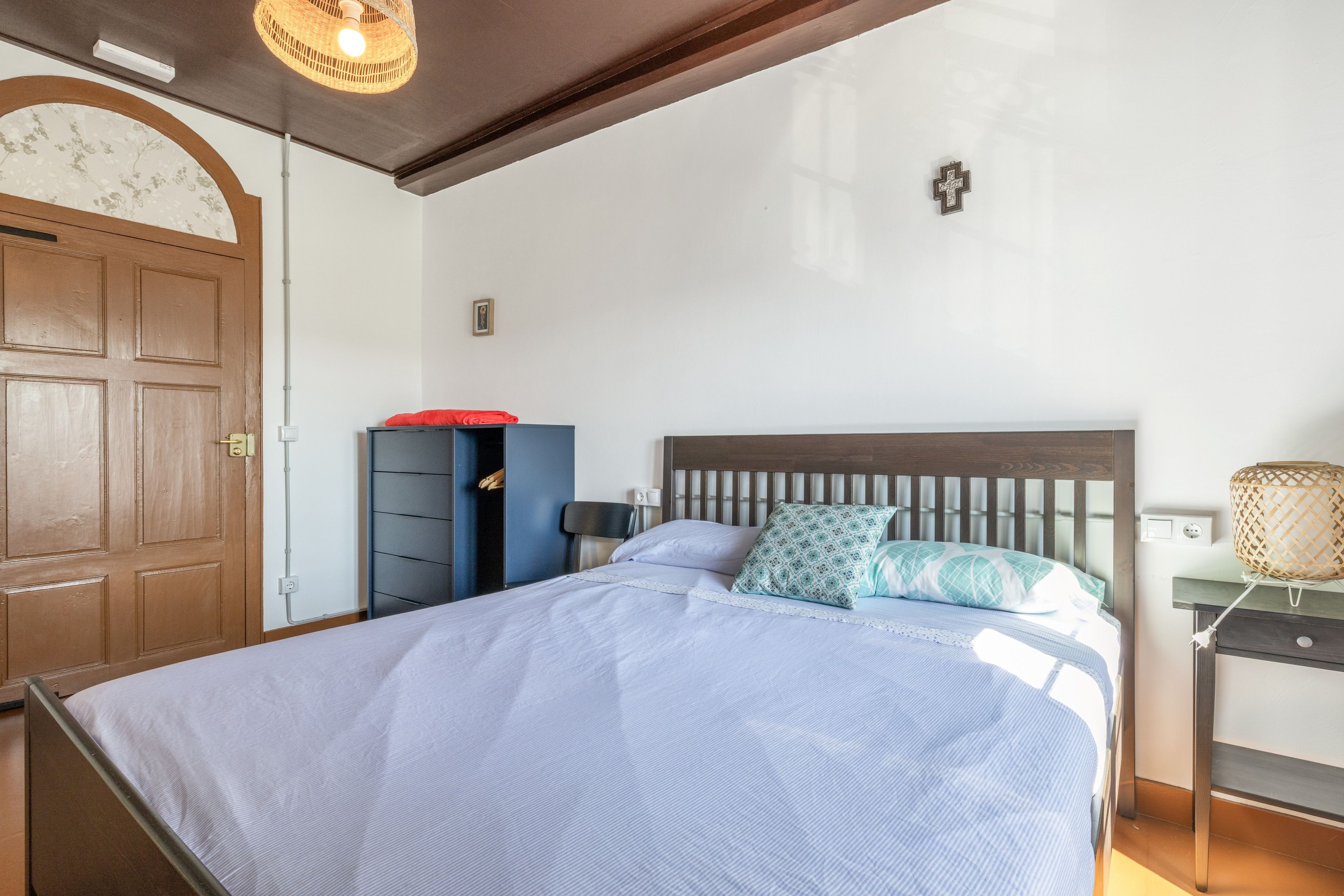 A bedroom with a bed, a wardrobe, a nightstand, and a wall-mounted lamp.