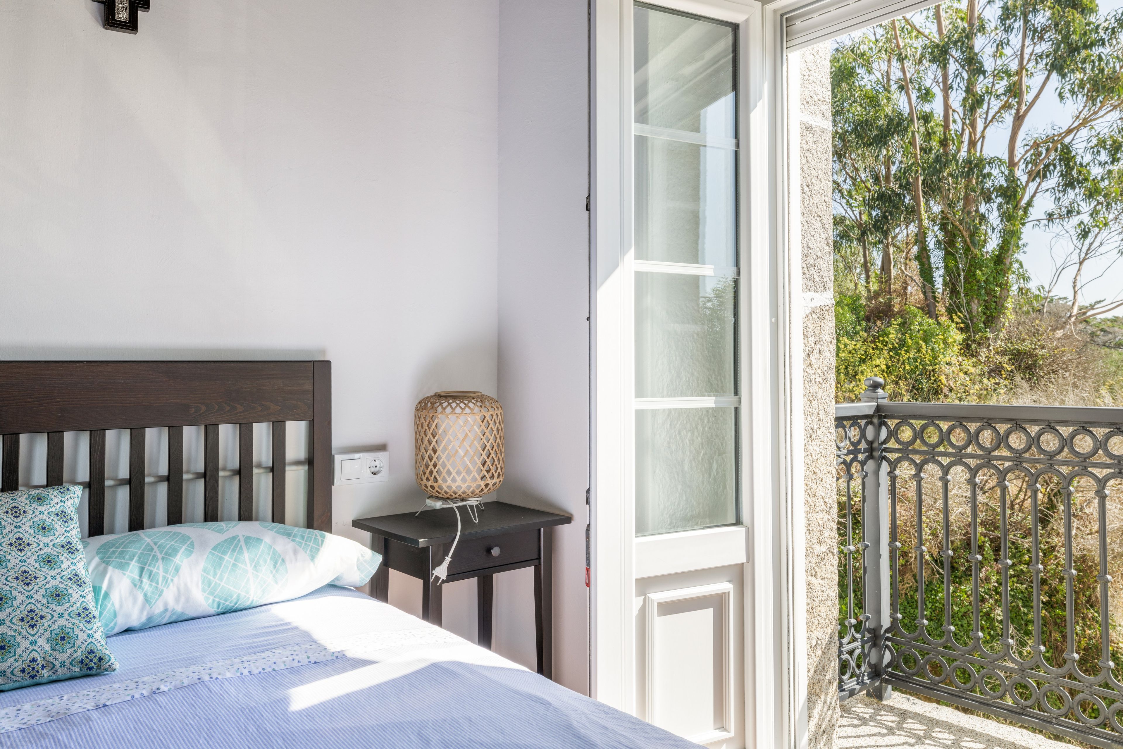 Un dormitorio con cama, mesita de noche, lámpara y vistas al exterior.