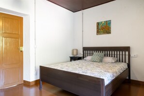 Een slaapkamer met een houten bed, een nachtkastje, een lamp en een schilderij aan de muur.