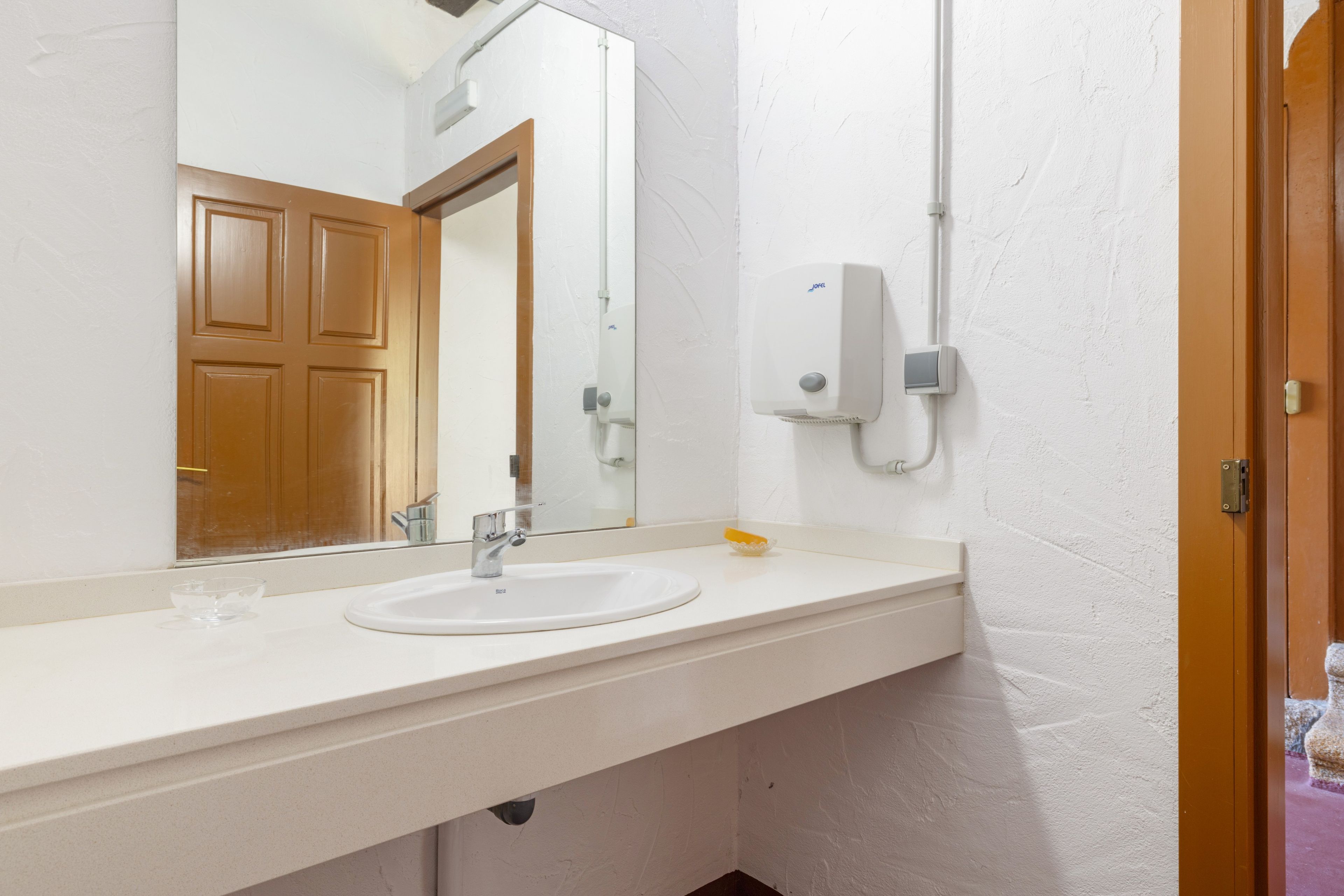Un bagno con un lavandino bianco, uno specchio e un dispenser di sapone a parete.