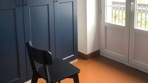 Huoneessa on tummansininen vaatekaappi, musta tuoli ja valkoinen ovi, jossa on ikkuna.