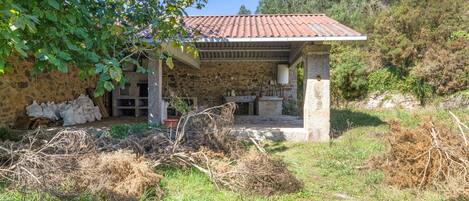 Una casa de piedra con tejado de baldosas, un porche cubierto y un muro de piedra.