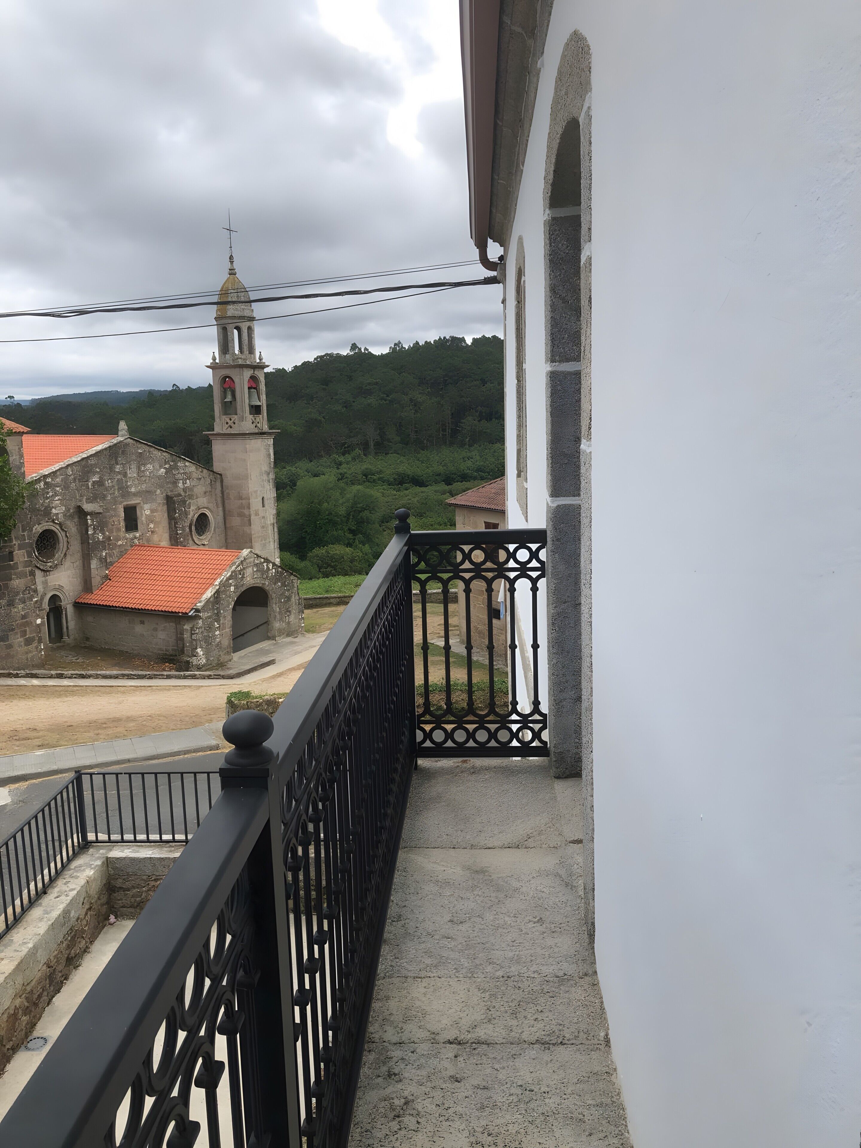 A balcony with a metal railing overlooking a building with a bell tower and a red-tiled roof.