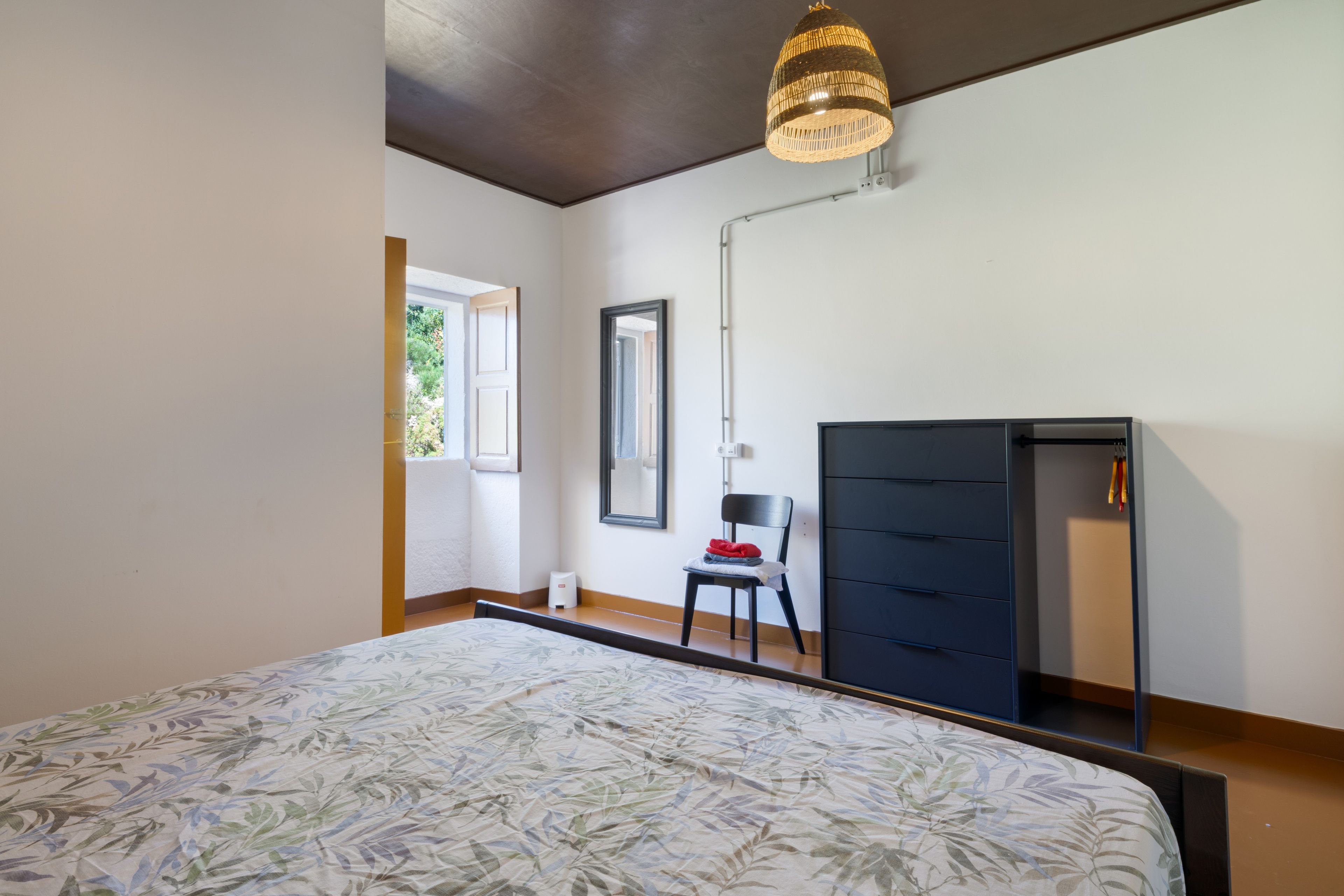 A bedroom with a bed, a chair, a dresser, and a hanging light fixture.